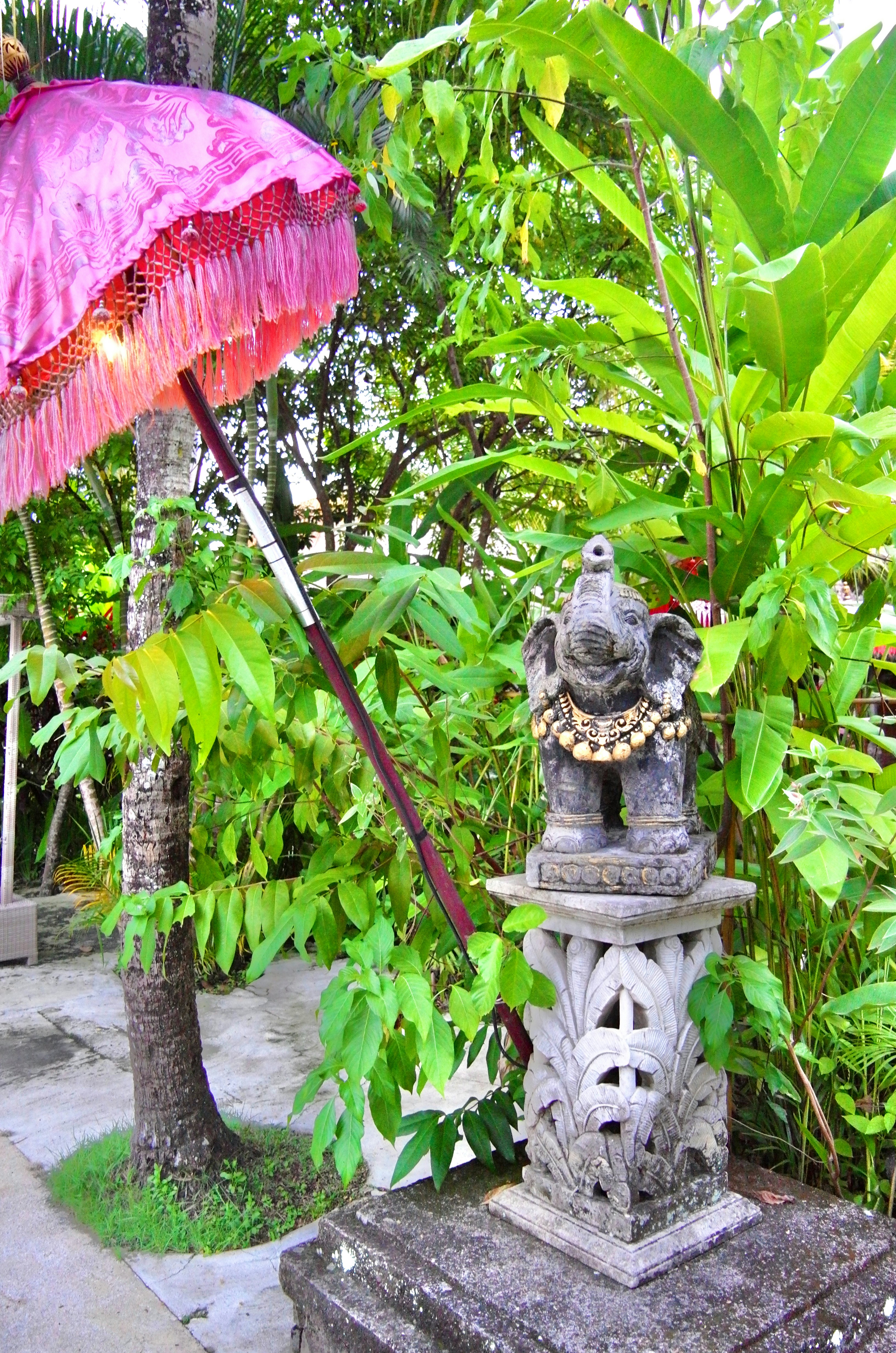 a stone statue with a pink umbrella in a garden