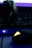 A close-up of a gaming setup, featuring a headset placed on a keyboard and a gaming mouse with an illuminated emblem. The lighting is dim, with a strong emphasis on the neon blue and yellow accents on the devices.