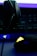 A close-up of a gaming setup, featuring a headset placed on a keyboard and a gaming mouse with an illuminated emblem. The lighting is dim, with a strong emphasis on the neon blue and yellow accents on the devices.