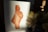 A watercolor painting on paper showing an abstract form with a curvy shape, primarily in shades of brown. The painting is on a white piece of paper, standing on a dark surface. Beside the paper is a ceramic vase containing yellow and white flowers illuminated by a soft light.