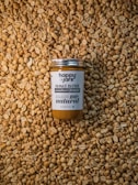A jar of peanut butter labeled 'Happy Jars' and '100% natural' is centered on a large pile of unshelled peanuts. The design of the jar emphasizes its natural and preservative-free qualities.