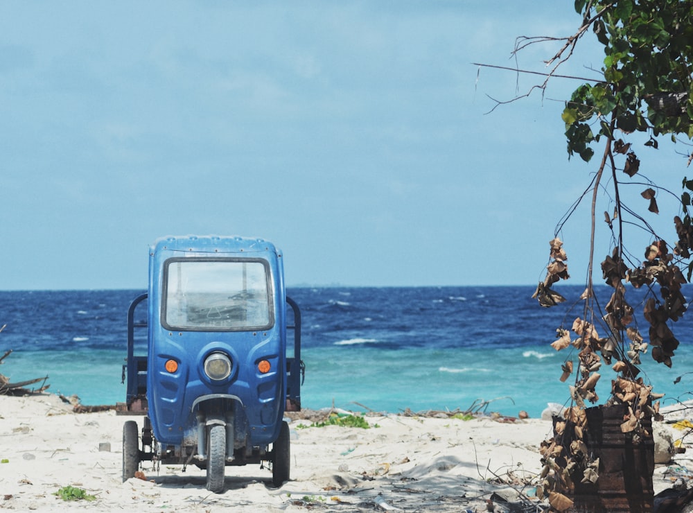 a small blue vehicle parked on a sandy beach