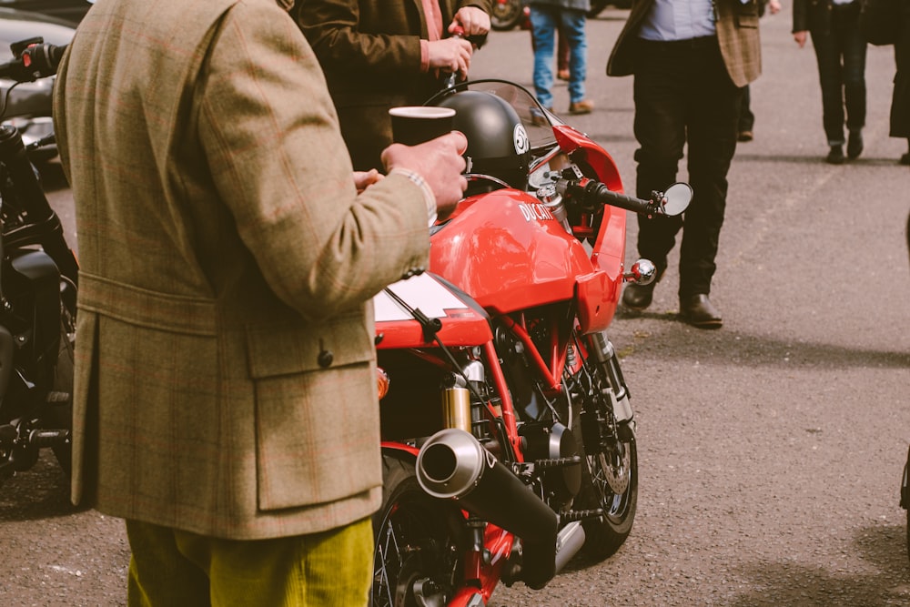 a man in a suit standing next to a red motorcycle