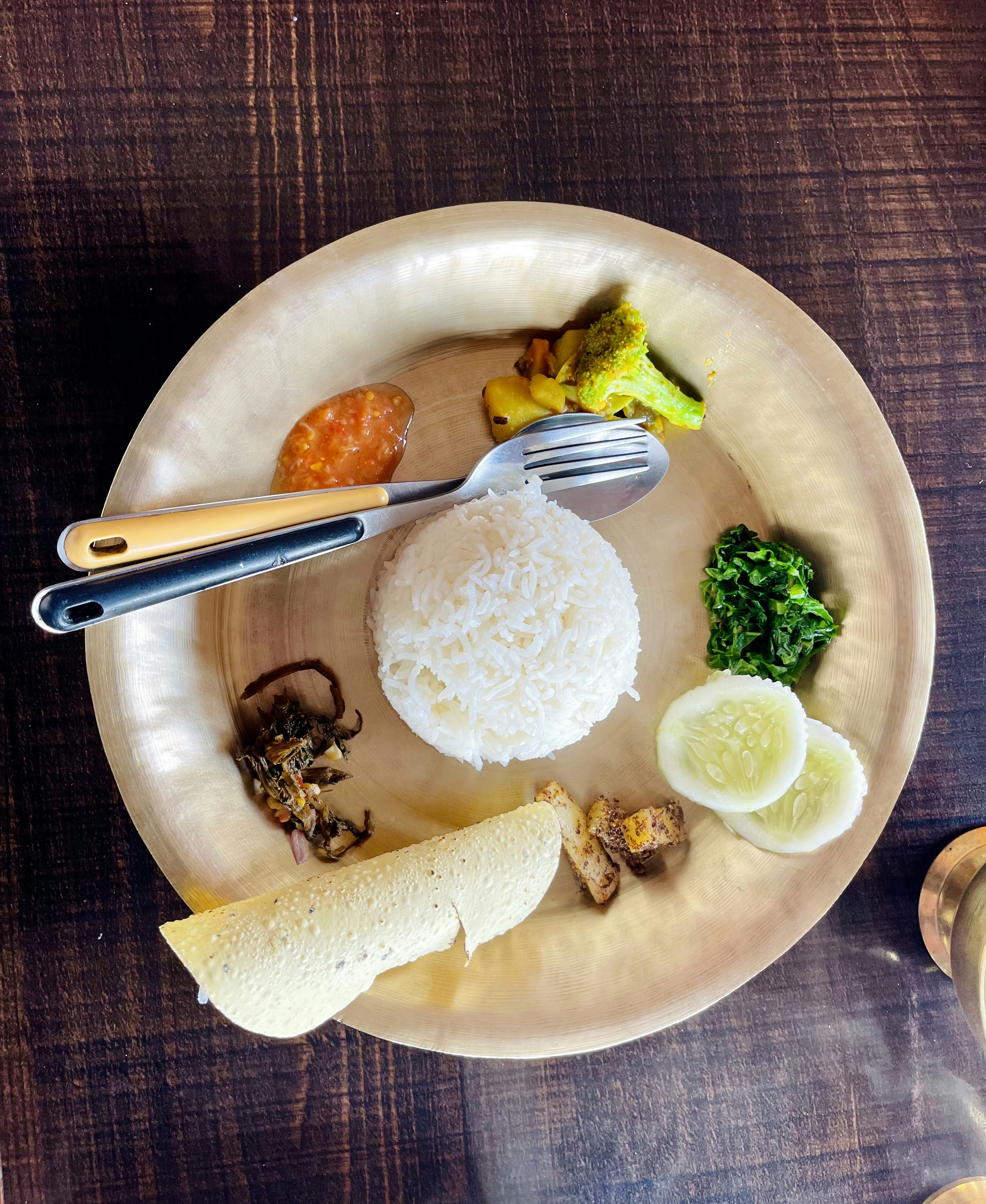 Top-down view of a full Malvani thali with rice, multiple curries, papad and pickle — dark wooden table