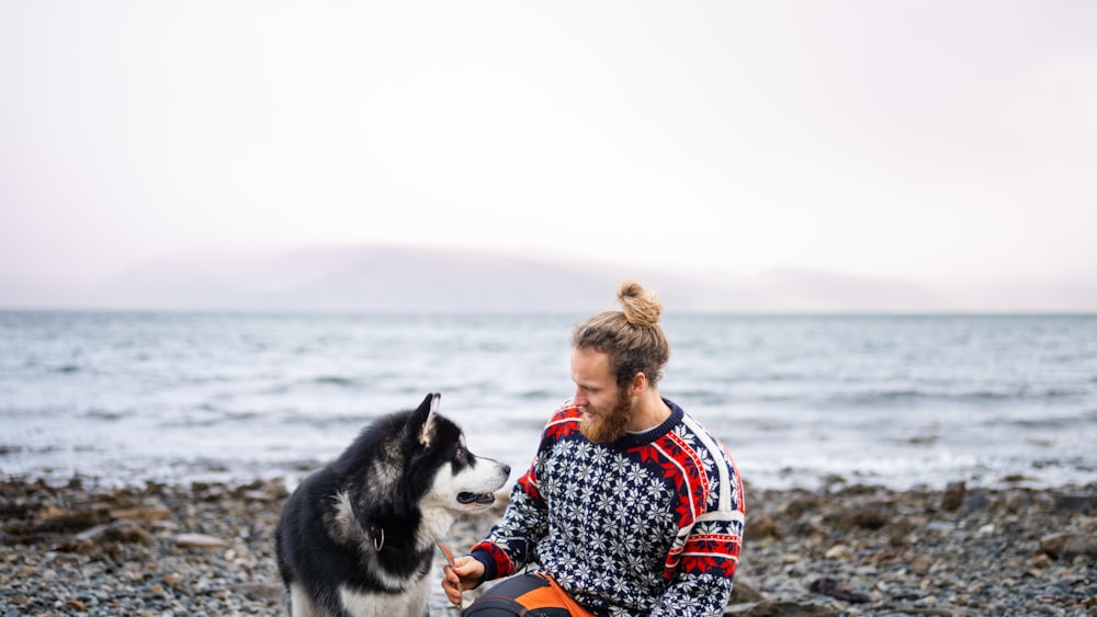 a man sitting on a rocky beach next to a dog