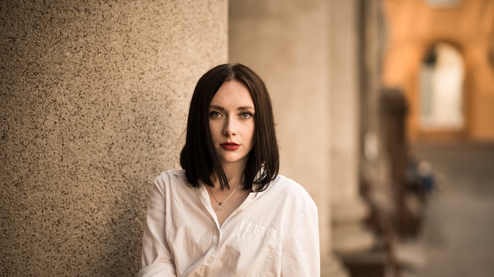 a woman leaning against a wall in a white shirt