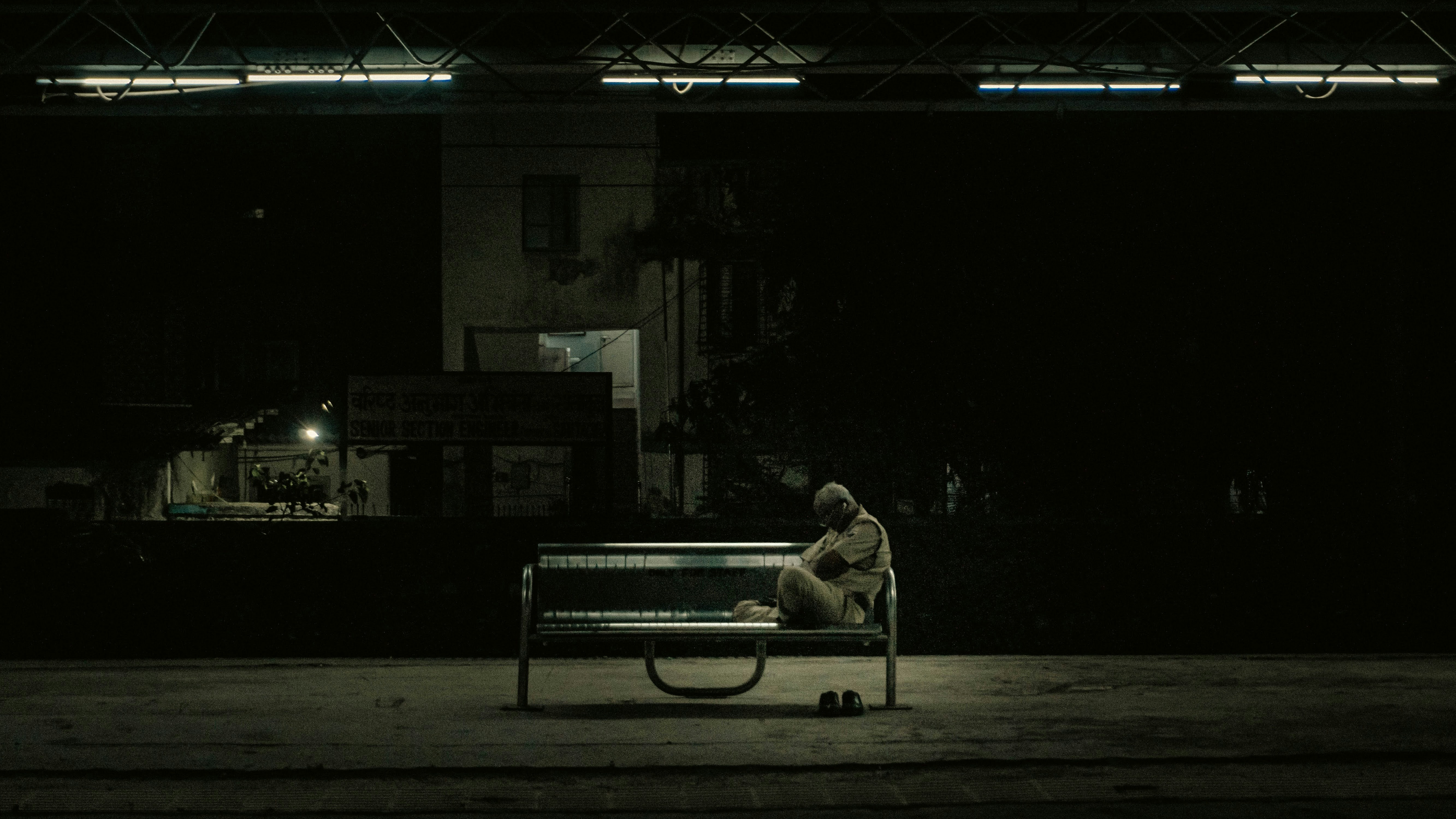 a solitary person sitting on a bench at night looking at the city lights
