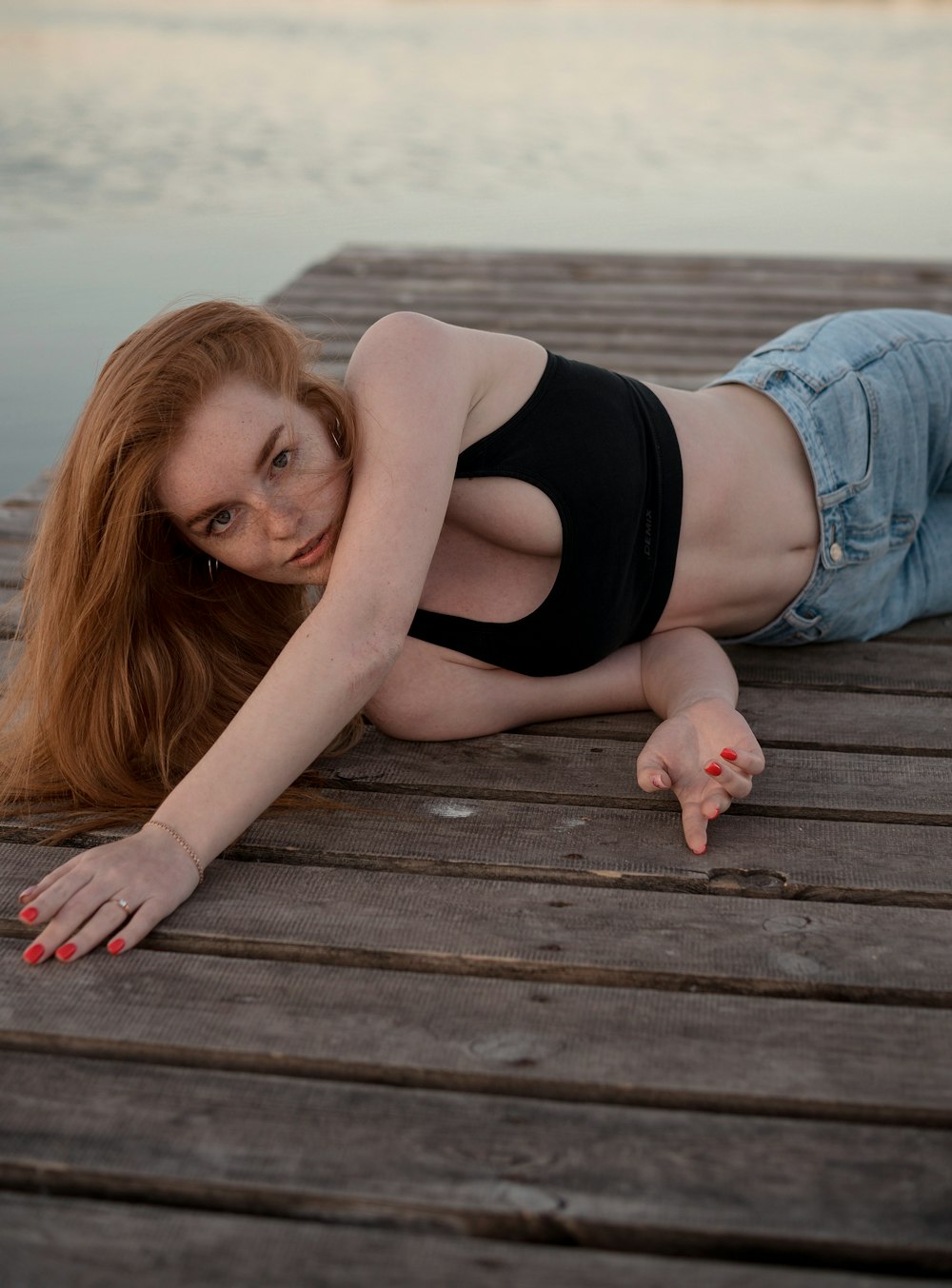 a woman laying on a wooden dock next to a body of water