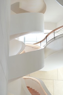 A minimalist architectural detail of a sleek, copper-toned spiral staircase bathed in soft natural light.