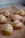 A close-up view of several freshly baked pastries topped with sesame seeds, arranged on a baking tray lined with parchment paper. The pastries have a golden-brown crust with visible layers of flaky dough.