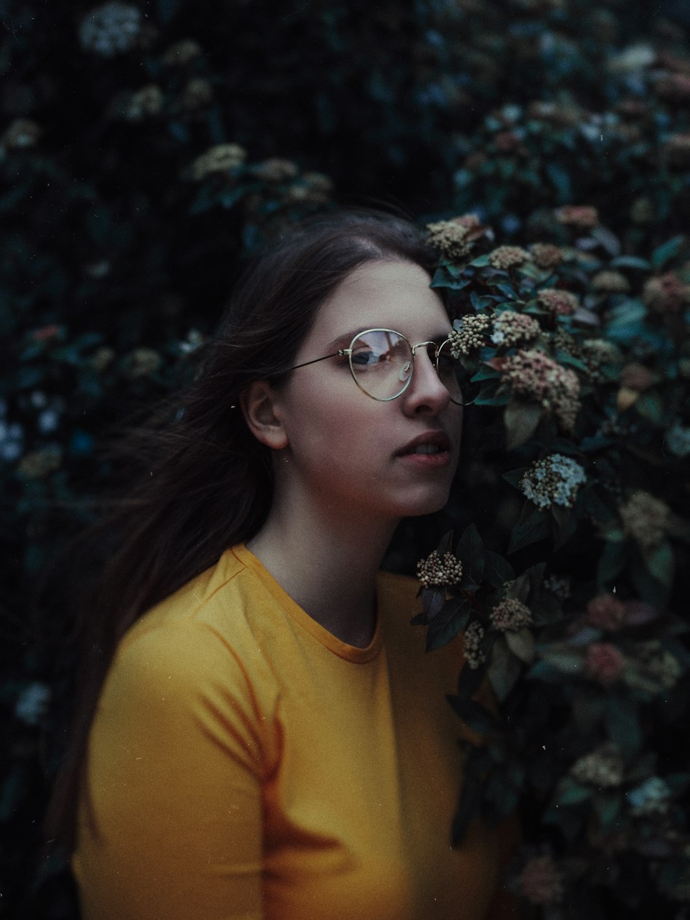 a woman wearing glasses standing in front of a bush