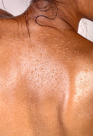 A person's back covered in small beads of sweat with dark hair strands