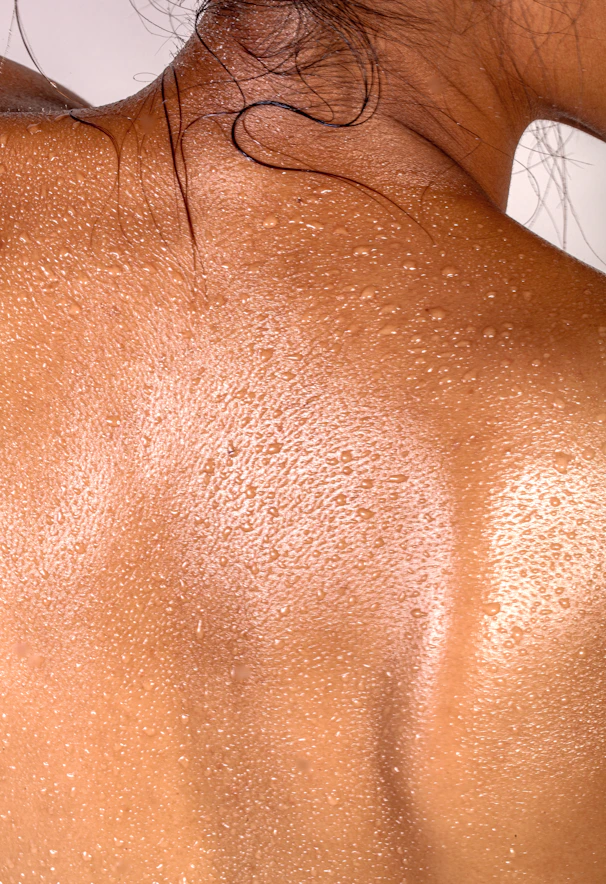 A person's back covered in small beads of sweat with dark hair strands