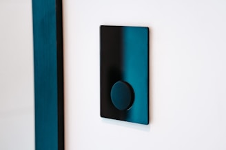 A modern black light switch is mounted on a white wall. The switch features a sleek, flat rectangular design with a circular button in the center.