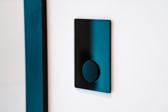 A modern black light switch is mounted on a white wall. The switch features a sleek, flat rectangular design with a circular button in the center.