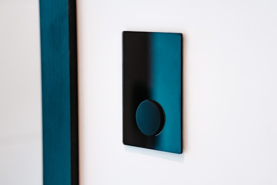 A modern black light switch is mounted on a white wall. The switch features a sleek, flat rectangular design with a circular button in the center.