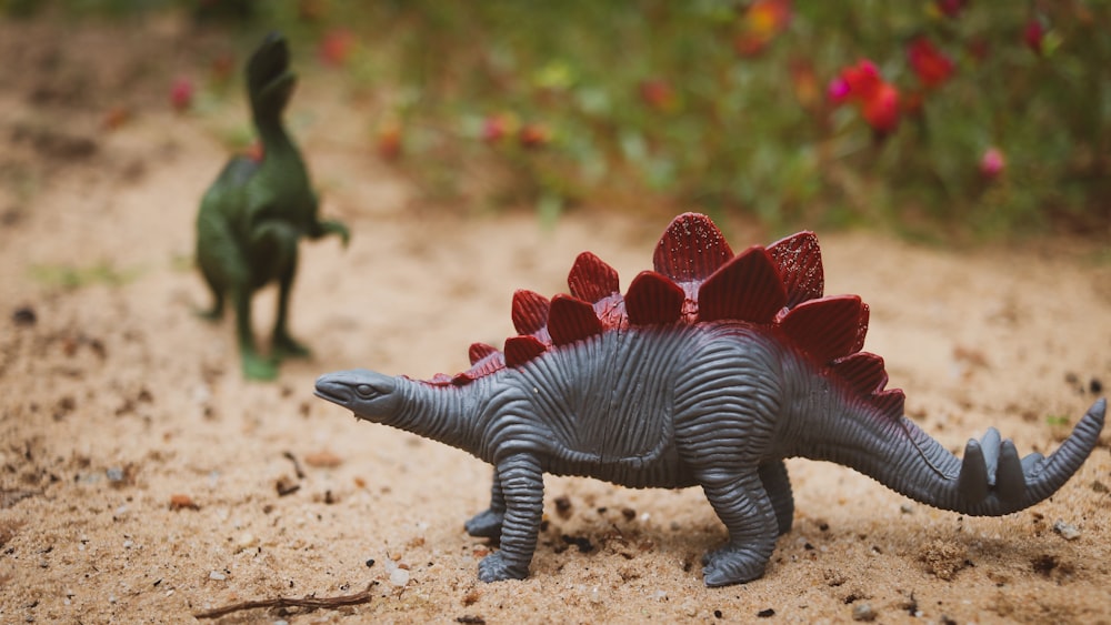 two toy dinosaurs walking on a dirt path