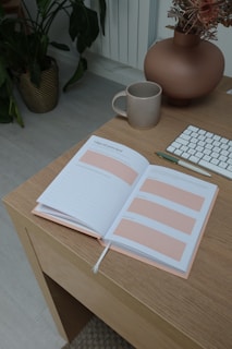 A serene workspace featuring a cozy desk with a journal, a cup of tea, and soft pink flowers in a vase.