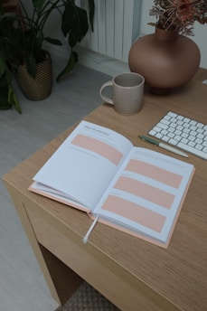 A serene workspace featuring a cozy desk with a journal, a cup of tea, and soft pink flowers in a vase.
