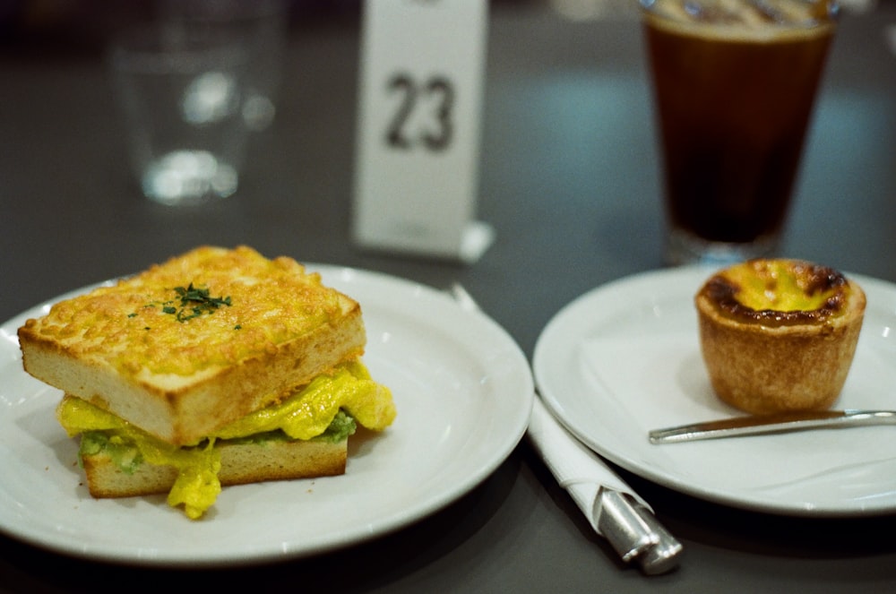 zwei Teller mit belegten Brötchen und einem Muffin auf einem Tisch