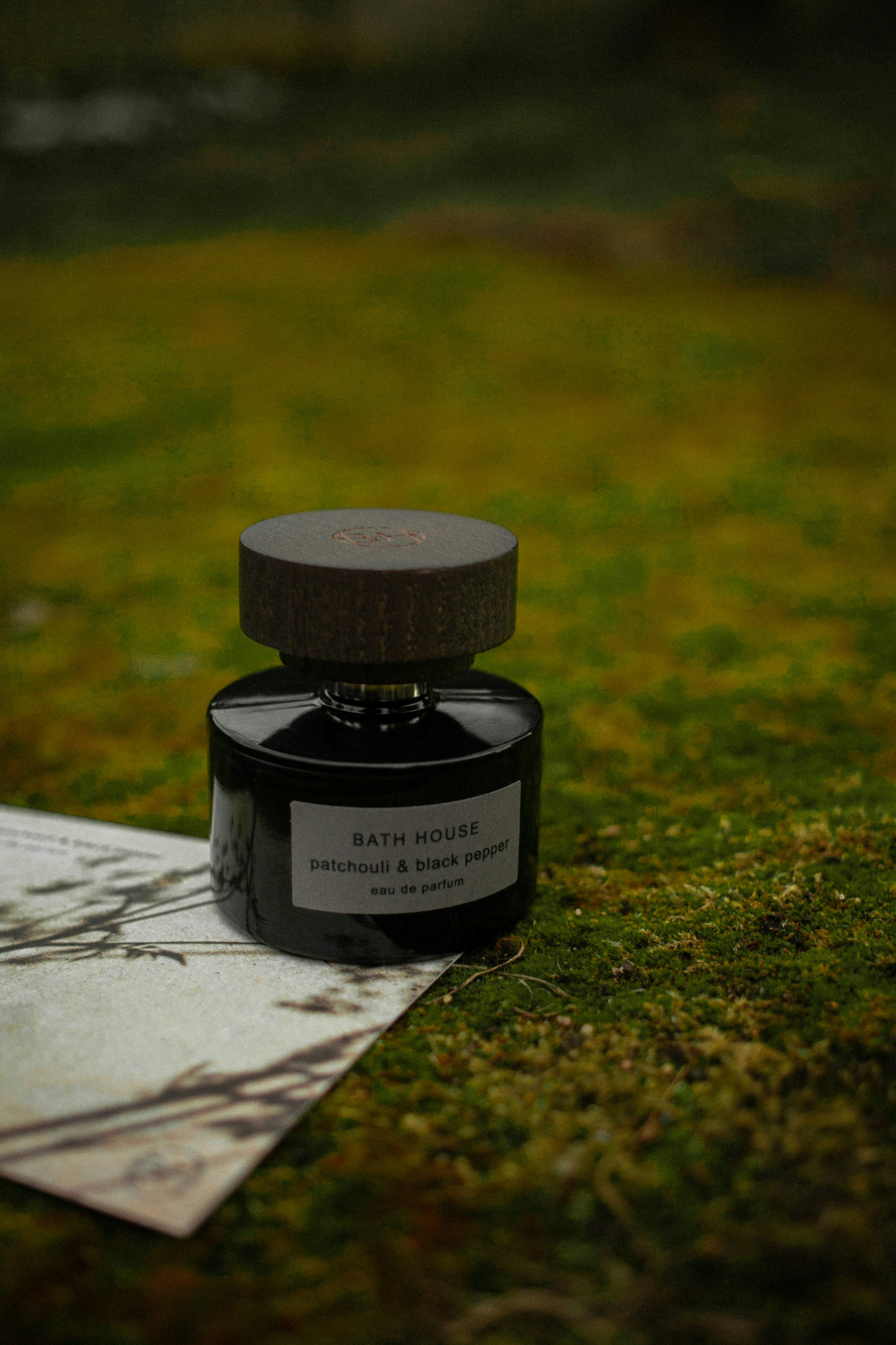 Dark masculine perfume bottle on rough stone surface, moody forest atmosphere, deep shadows and dramatic lighting