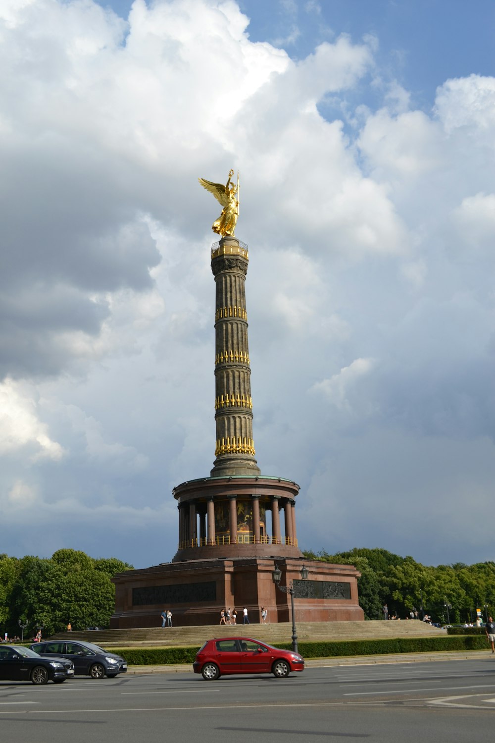 a red car parked in front of a golden statue