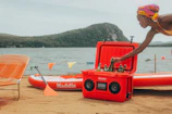 A portable wheeled cooler being pulled across a sandy beach with a family setting up a picnic nearby.