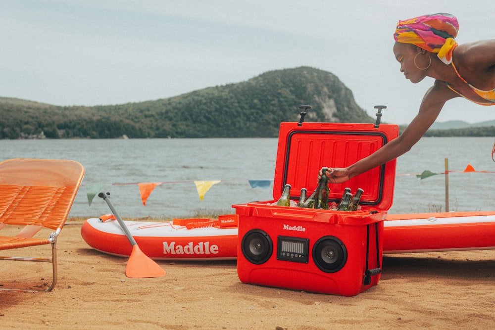 a woman leaning over a red cooler on the beach