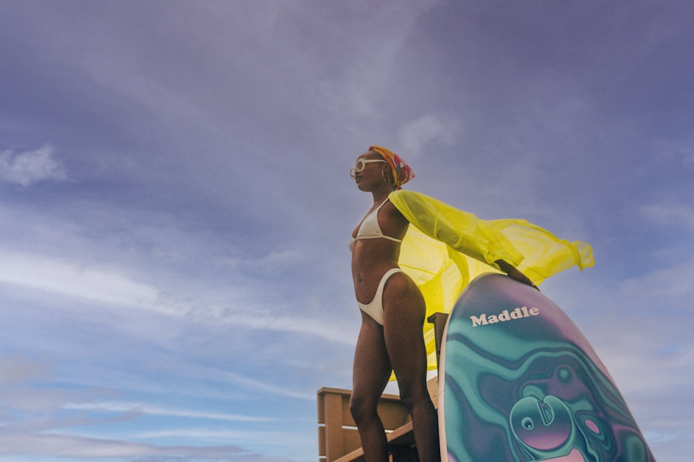 a woman in a bikini standing on a beach next to a surfboard