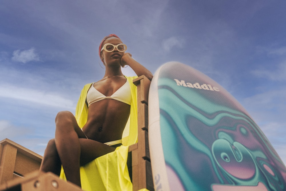 a woman in a bikini sitting next to a surfboard