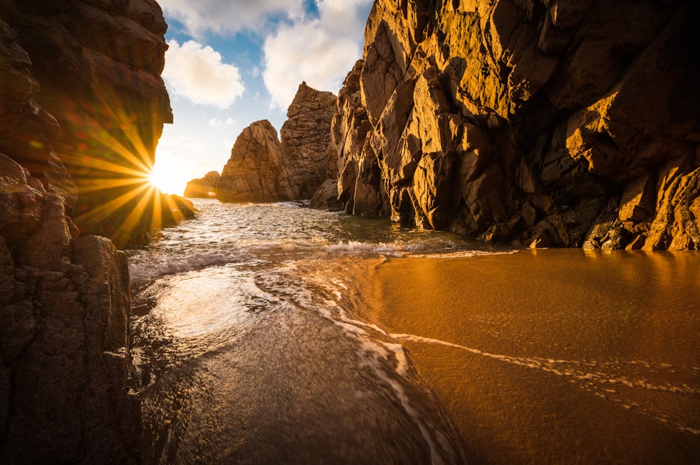 the sun shines brightly through the rocks on the beach