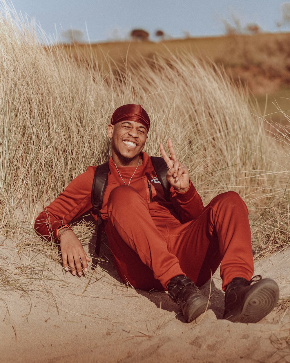 a man sitting in the sand making a peace sign