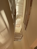 A modern architectural interior with curved and angled surfaces, featuring multiple balconies on different levels. The light cream colors and the play of light and shadows create an airy and spacious atmosphere.