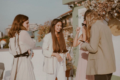 Women gathered in a circle on a sunlit terrace overlooking whitewashed Greek architecture.