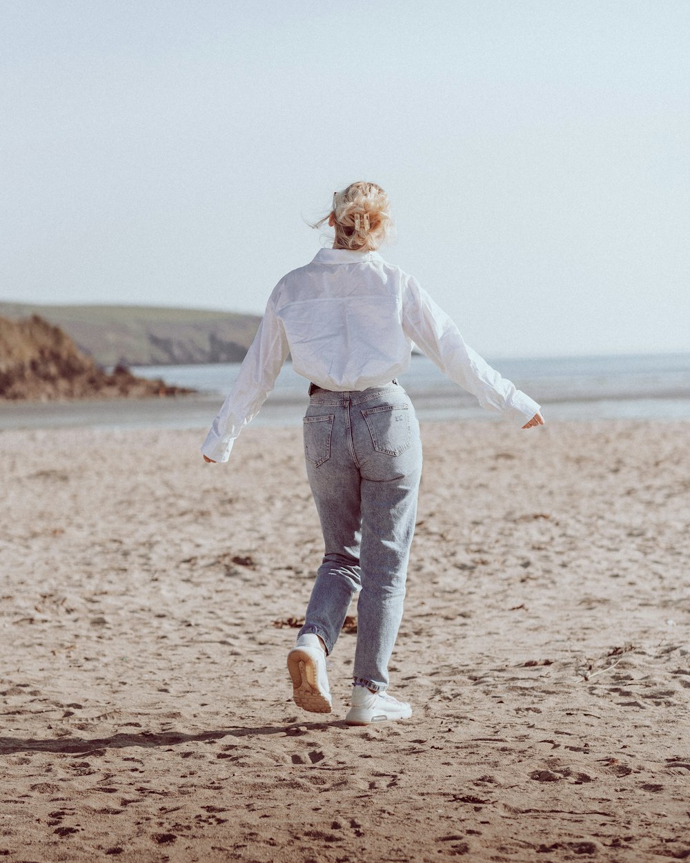 a woman walking across a sandy beach next to the ocean