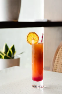 Tropical drink with layered colors and a slice of orange on the rim, set against a sunny beach scene