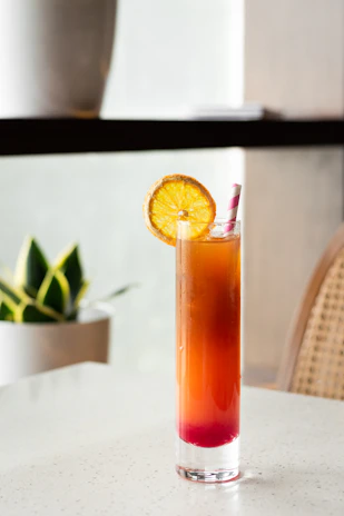 Tropical drink with layered colors and a slice of orange on the rim, set against a sunny beach scene
