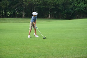 A young girl swinging a golf club with a big smile, her donated clubs lined up behind her on a sunny course.