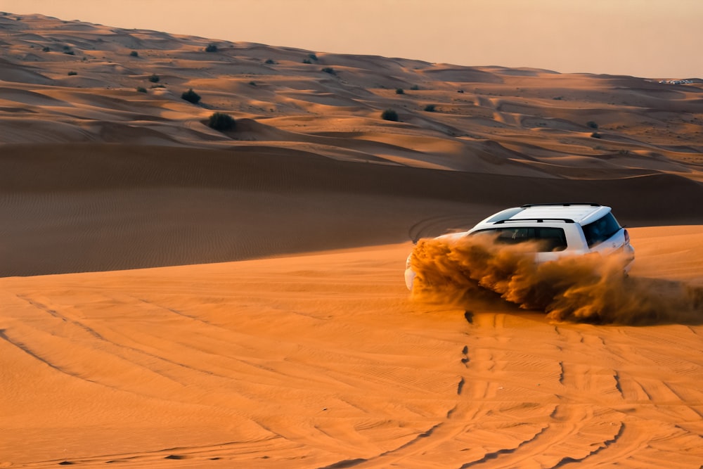 a white car driving through the sand dunes