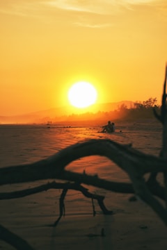 the sun is setting over the water on the beach