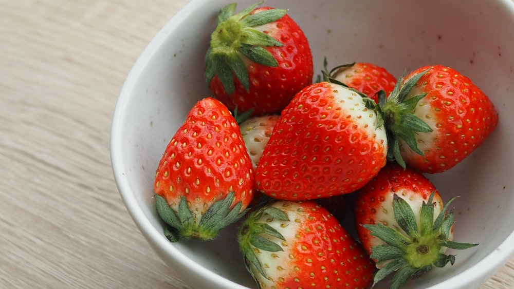 a white bowl filled with lots of ripe strawberries