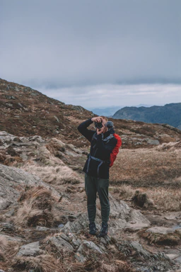 A candid photo of a traveler with a camera, standing on a misty Scottish hillside at dawn.
