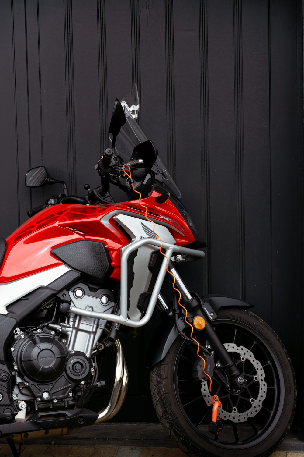 a red and white motorcycle parked next to a black wall