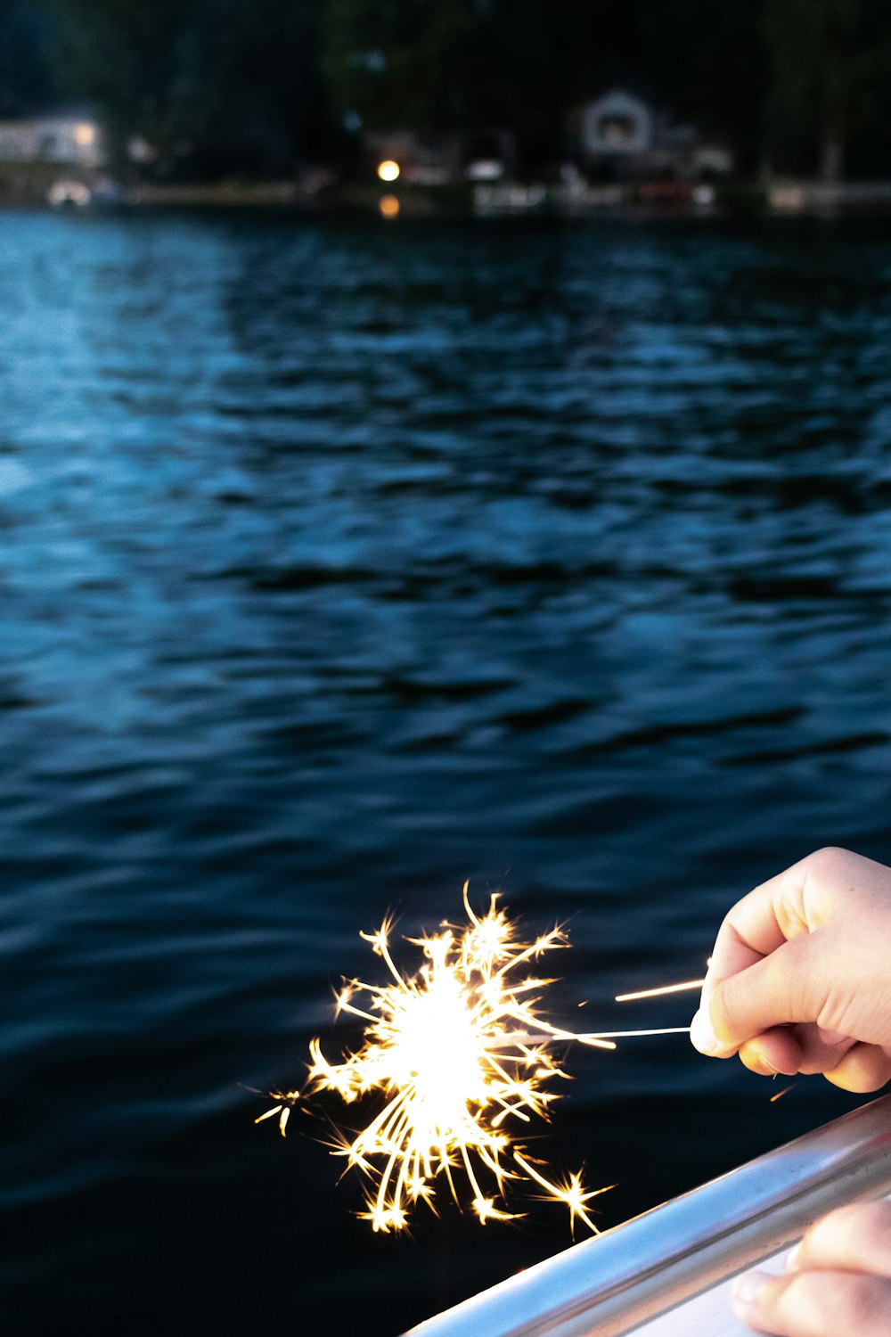 a hand holding a sparkler in front of a body of water