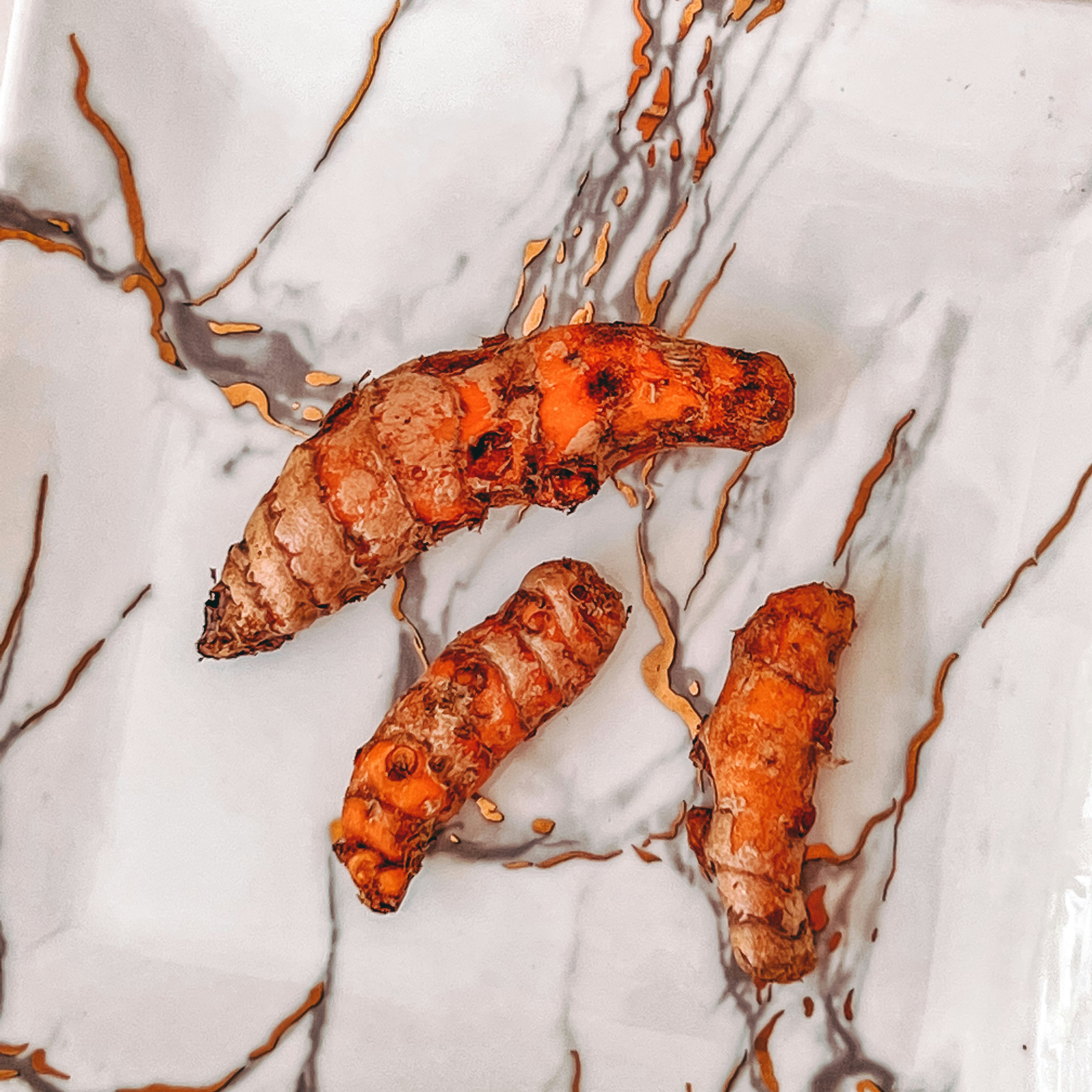 Fresh turmeric root and powder on bright white marble surface, warm golden tones, natural daylight