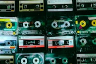 A collection of vintage cassette tapes is neatly arranged in rows, showcasing different brands such as Memorex, Sony, and TDK. Each tape displays handwritten labels with artist names and titles, reflecting a nostalgic appreciation for analog music formats.