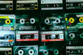 A collection of vintage cassette tapes is neatly arranged in rows, showcasing different brands such as Memorex, Sony, and TDK. Each tape displays handwritten labels with artist names and titles, reflecting a nostalgic appreciation for analog music formats.
