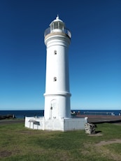 a white lighthouse on a grassy hill