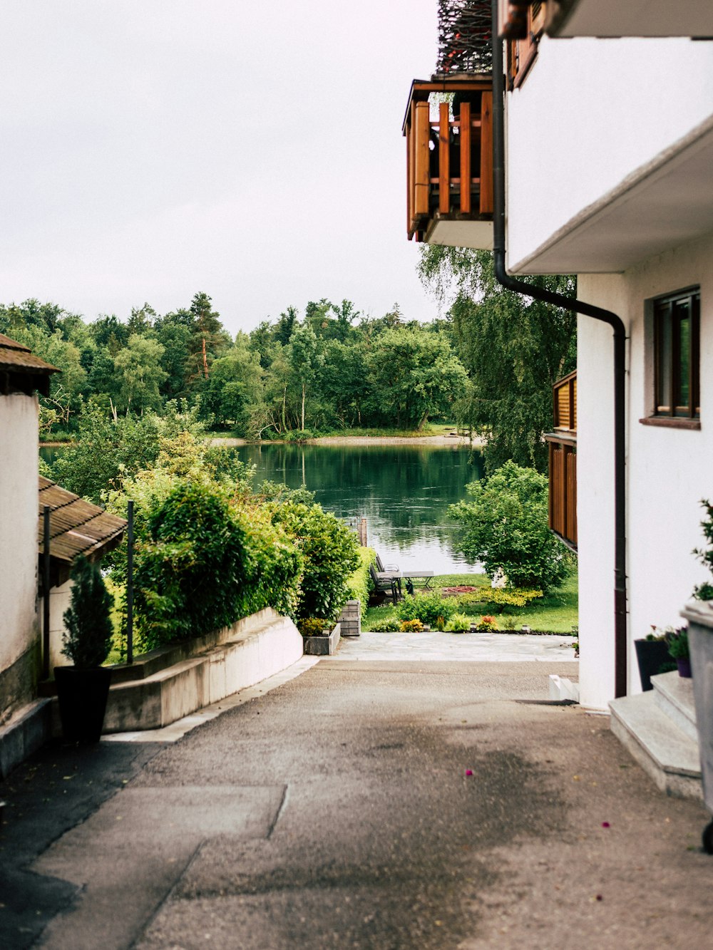 a path between buildings with trees and a body of water in the background