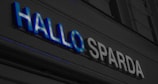 A sign with the words 'HALLO SPARDA' in large letters. The text is illuminated, with 'HALLO' in blue and 'SPARDA' in white. It appears to be part of a building facade.